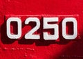 Weathered numbers zero, two, five, 0250, or 0, 2, 5 painted white on a piece of red metal. Abstarct numeral background.