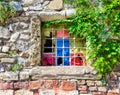 Weathered old stone bricks wall with corroded antique grunge wrought iron window with multi vibrant colored squares Royalty Free Stock Photo