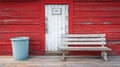 A weathered red barn with a rustic door, situated in a rural area, featuring an old bin and a bench Royalty Free Stock Photo