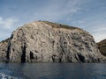 Weathered seaside rock face texture with parts of green and blue water. Aged volcanic stone wall surface background Royalty Free Stock Photo