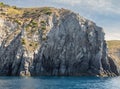 Weathered seaside rock face texture with parts of green and blue water. Aged volcanic stone wall surface background pattern Royalty Free Stock Photo