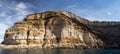 Weathered seaside rock face texture with parts of green and blue water. Aged volcanic stone wall surface Royalty Free Stock Photo