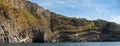 Weathered seaside rock face texture with parts of green and blue water. Aged volcanic stone wall surface Royalty Free Stock Photo