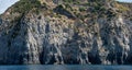 Weathered seaside rock face texture with parts of green and blue water. Aged volcanic stone wall surface background Royalty Free Stock Photo