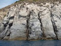 Weathered seaside rock face texture with parts of green and blue water. Aged volcanic stone wall surface background Royalty Free Stock Photo