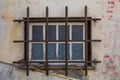 A weathered window with peeling white paint and patterned glass is secured by a rusty metal grille Royalty Free Stock Photo