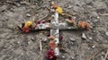 A weathered wooden cross lies on the ground nearby adorned with dried flowers and feathers in a solemn homage to the