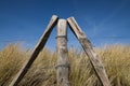 weathered wooden stakes from a fence stand in a triangle in front of the sand dunes with marran grass on the beach of the Baltic