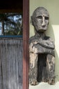 Weathered wooden statue by a yellow wall and an open door with bamboo fence