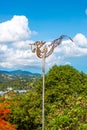 Weathervane forged cockerel on a pole against the backdrop of a tropical vertical landscape