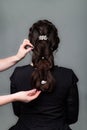 Weave, braid tail hairstyle. Hairdresser making hairstyle to brown hair woman with long hair on a gray background. Professional Royalty Free Stock Photo