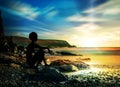 Girl silhouette sitting alone on rocks, stones on shore of the water Royalty Free Stock Photo