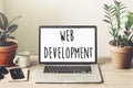 web development text on laptop screen on wooden desktop with phone, notebook, coffee and plant. web design online technology. Royalty Free Stock Photo