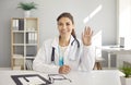 Webcam portrait of happy female online doctor sitting at desk, smiling and waving hello Royalty Free Stock Photo