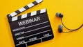 Webinar invitation is shown by a clapperboard with the word WEBINAR and a pair of in-ear headphones on a yellow background Royalty Free Stock Photo