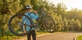 Website header of Strong athletic man in sportswear holding a bicycle while standing in park at sunset, cycling outdoors Royalty Free Stock Photo
