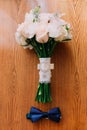 Wedding accessories: bow tie of groom, bridal white roses bouquet on the wooden table Royalty Free Stock Photo