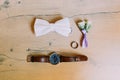 The wedding accessories. The lovely rose boutonniere, hand watch, silver ring and bow-tie on the rustic floor.