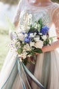 The bride is holding a bouquet of the bride from white roses, white daisies, blue flowers, fern leaves and other flowers
