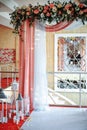 Wedding arch draped with white and pink fabric, white and red flowers on the top, decorative lamps with candles on the sides