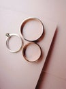 Wedding band and golden engagement ring on rosy paper background, close up, flat lay