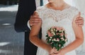 Wedding blonde couple is kissing in old city. Groom and bride in lace satin dress with pink rose bouquet are near the ancient