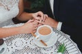 Wedding blonde couple is sitting in vintage cafe outdoors. Groom and bride in lace satin dress are holding hands and drinking Royalty Free Stock Photo