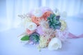 Wedding bouquet featuring trendy succulents, peachy peonies, white tulips, and ivory roses, embellished with ribbons