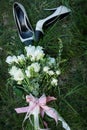 Wedding bouquet. Female fashion beige and black wedding shoes with bride`s bouquet of white roses and greenery on green grass back Royalty Free Stock Photo