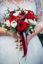 Wedding bouquet of fresh flowers in bride`s hands, cropped image, close-up. Young bride holding a bouquet of white and red roses Royalty Free Stock Photo