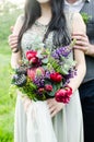 Wedding bouquet with green, red and violet flowers and white ribbon. Bride and groom with wedding bouquet in her hands. Royalty Free Stock Photo