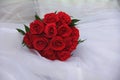 A wedding bouquet of red roses lies on a white pillow