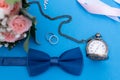 Wedding bouquet and wedding rings on a background of blue paper with a man`s butterfly and an old clock on a chain