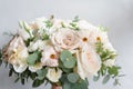 Wedding bouquet of white roses and buttercup on a wooden table. Lots of greenery, modern asymmetrical disheveled bridal