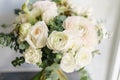 Wedding bouquet of white roses and buttercup on a wooden table. Lots of greenery, modern asymmetrical disheveled bridal