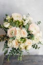 Wedding bouquet of white roses and buttercup on a wooden table. Lots of greenery, modern asymmetrical disheveled bridal