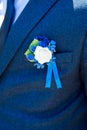 Wedding boutonniere of white rose, small blue flowers, berries and ribbon pinned to the dark blue jacket of the groom.