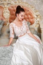 Wedding. Bride in beautiful dress sitting on sofa in white studio interior like at home. Trendy wedding style Royalty Free Stock Photo