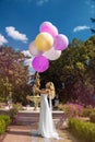 Wedding. Bride in a beautiful dress, standing in a beautiful garden and holding balloons. Trendy wedding style shot in full length