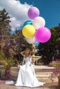 Wedding. Bride in a beautiful dress, standing in a beautiful garden and holding balloons. Trendy wedding style shot in full length