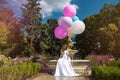 Wedding. Bride in a beautiful dress, standing in a beautiful garden and holding balloons. Trendy wedding style shot in full length