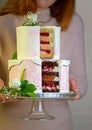 The girl cuts and serves a festive wedding two-tiered cake, decorated with fresh flowers on a gray background Royalty Free Stock Photo