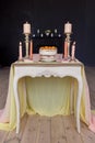 Wedding cake, candles in candlesticks and two glasses stand on a white vintage table decorated with a cloth Royalty Free Stock Photo