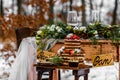 Wedding cake with fruit and an old wooden table with needles of cones and leaves during a wedding ceremony in winter on snow in