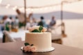 Wedding cake stands on the table against the backdrop of guests sitting at a table on the seashore