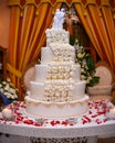 Wedding cake on a white table decorated with red roses. Wedding statues at the top of the cake