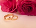 Wedding celebration with pink rose bouquet, gold wedding rings on pink background. Concept of love and romance