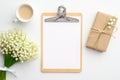 Wedding checklist concept. Clipboard with blank paper mockup, gift box wrapped craft paper, cup of coffee and lily of the valley