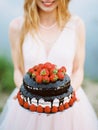 Smiling bride in white dress holding wedding chocolate cake with strawberries