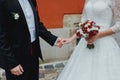 Wedding couple is hugging near the orange wall. Bride in lace satin dress is holding a bouquet of dark red marsala roses, peony Royalty Free Stock Photo